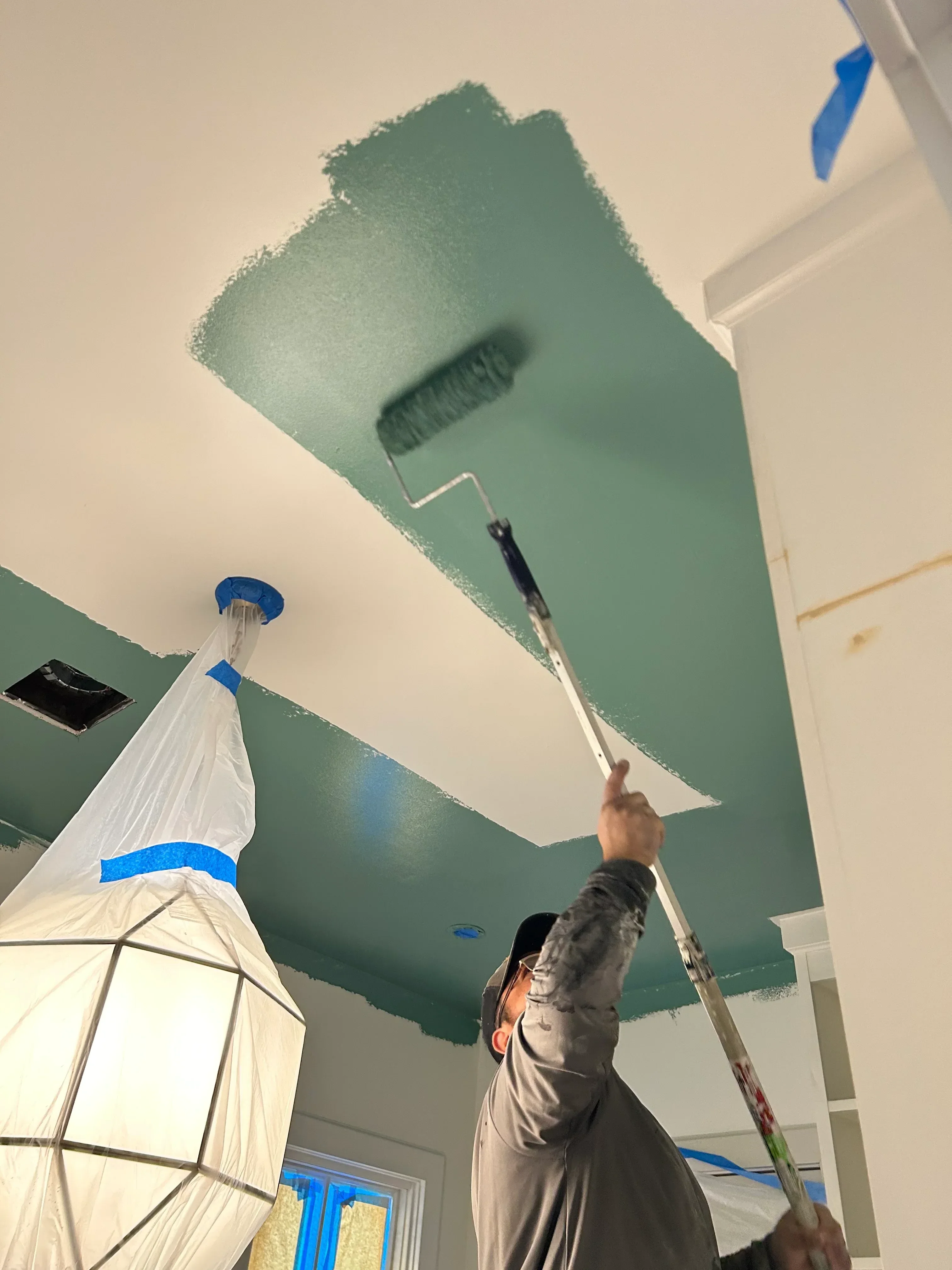 Painter applying sage green paint to interior wall with roller and brush
