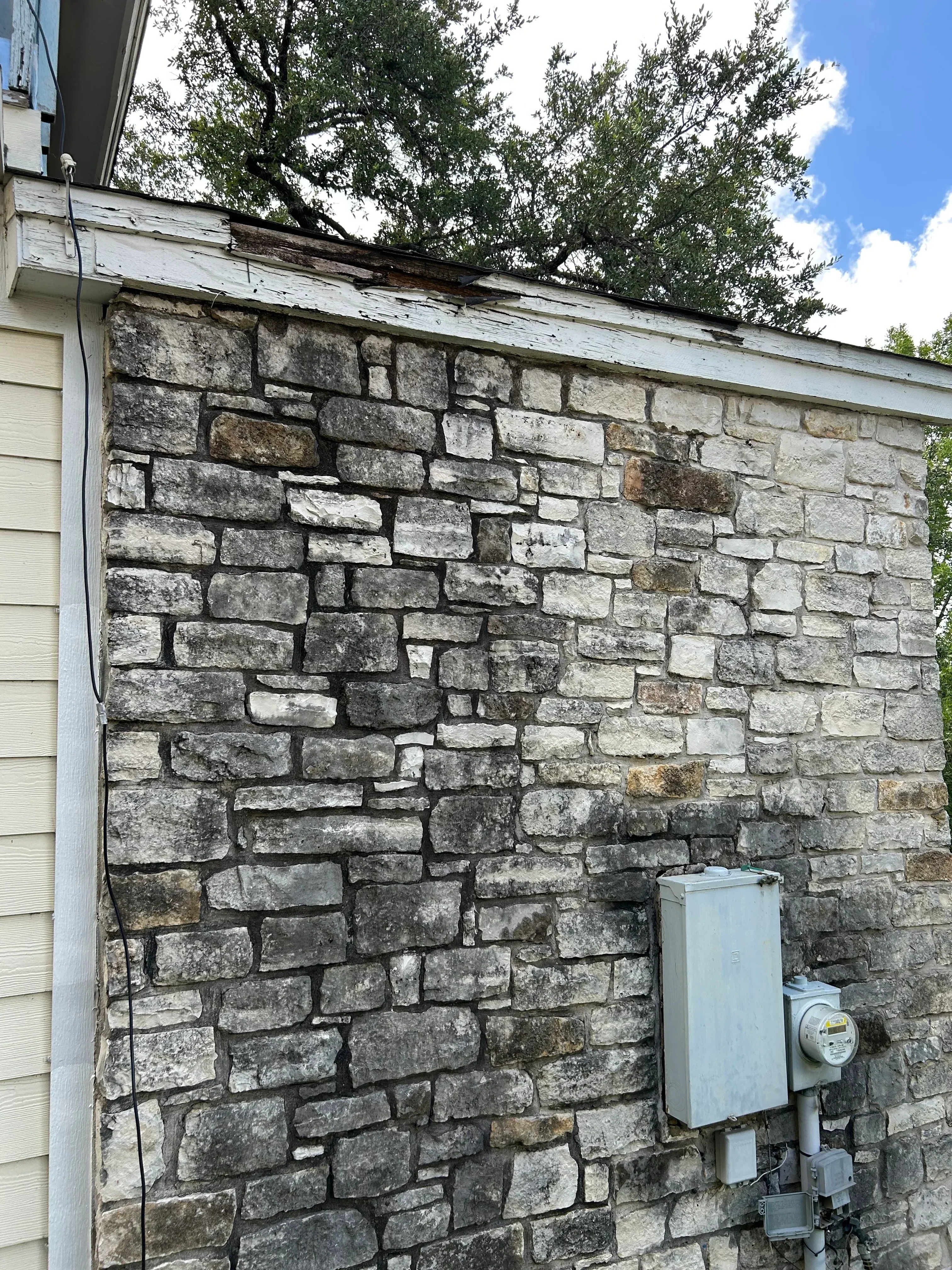 Weathered stone chimney with moss growth and aged masonry blocks, metal flashing and utilities visible