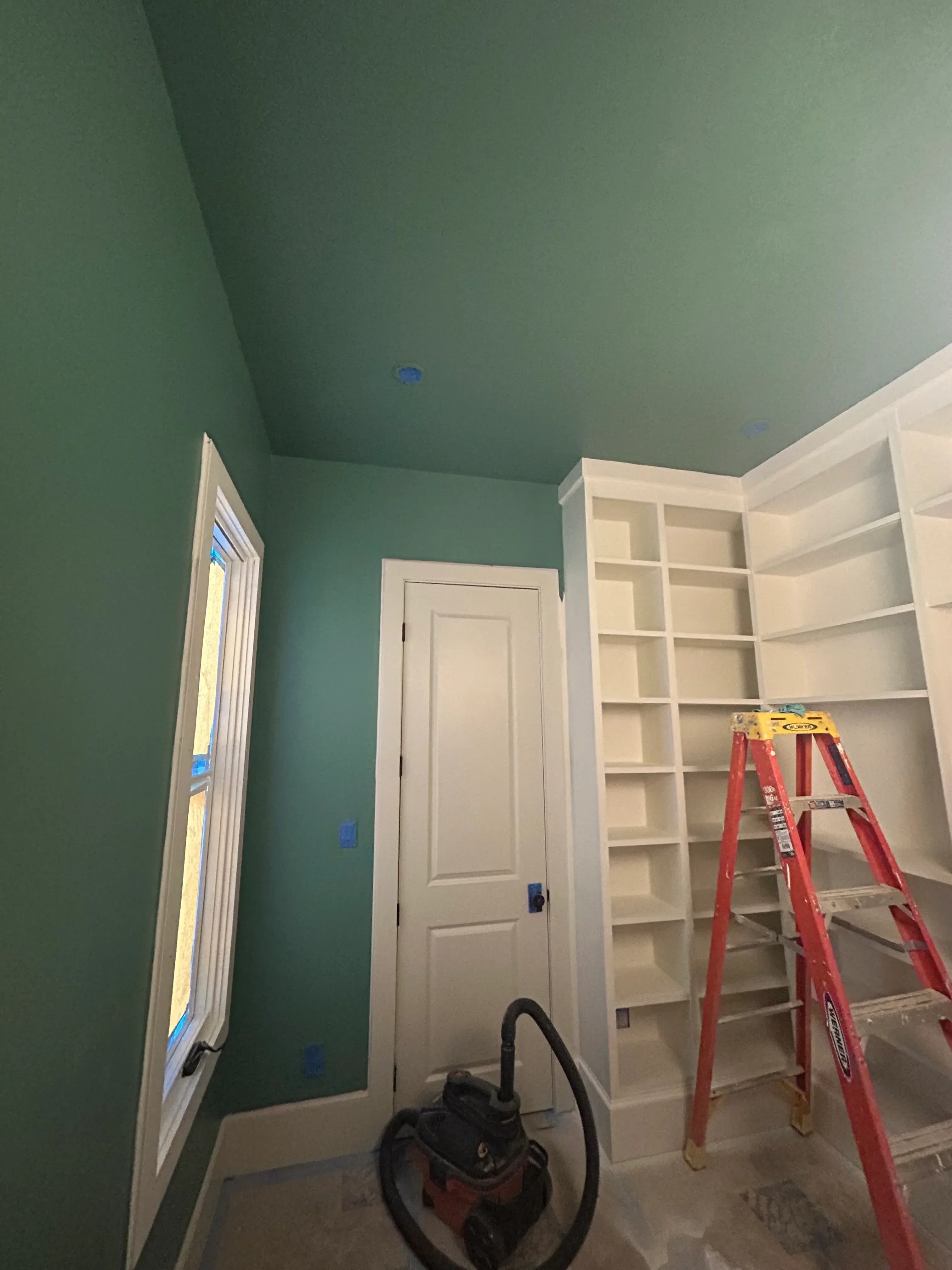 White built-in shelving unit with red support beams above garage door, green painted drywall walls