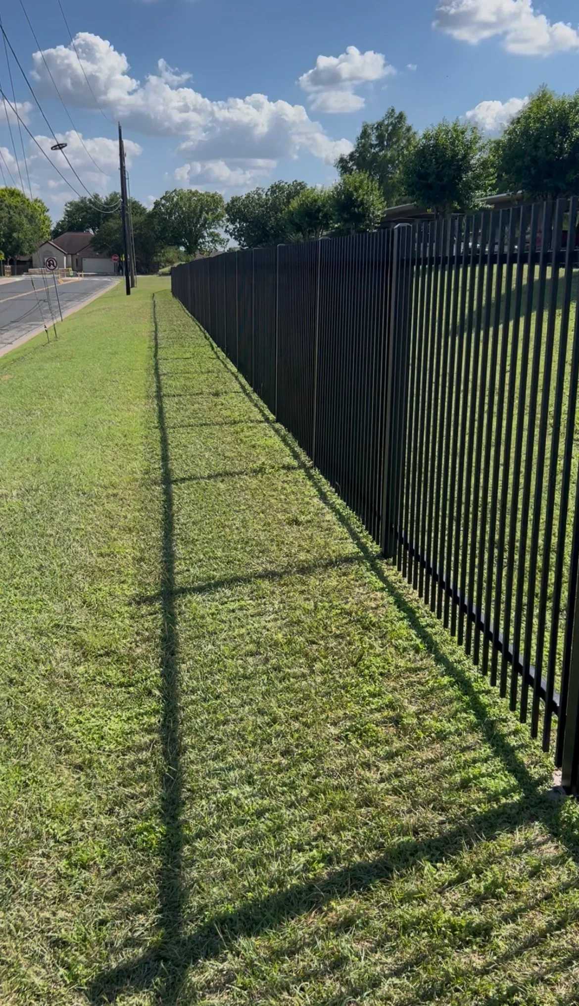 Black metal picket fence freshly painted along residential property with green lawn